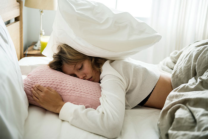 Woman sleeping with pillow on head, illustrating bridesmaid stress.