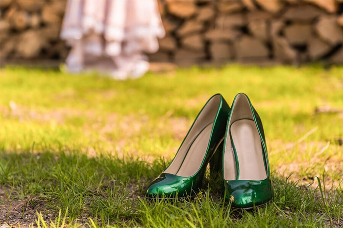 Green high heels on grass, with blurred bride's dress in background, showcasing bridesmaids' requests.