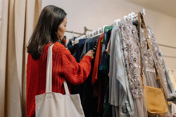 Woman shopping for dresses, browsing clothing rack, wearing red sweater, related to bridesmaid requests.