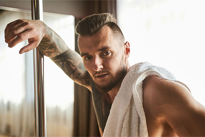 Man with tattoos and a towel posing confidently near a pole, representing unique bridesmaid requests.