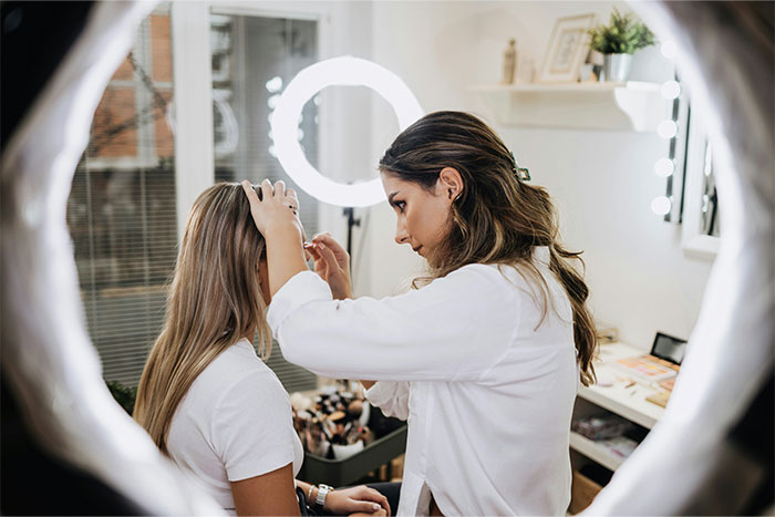 Woman adjusts another woman's hair in a well-lit room, highlighting bridesmaid preparation.