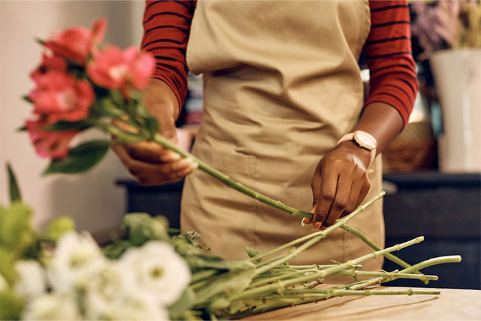 Bridesmaid arranging pink and white flowers, wearing a beige apron, in a floral workshop.