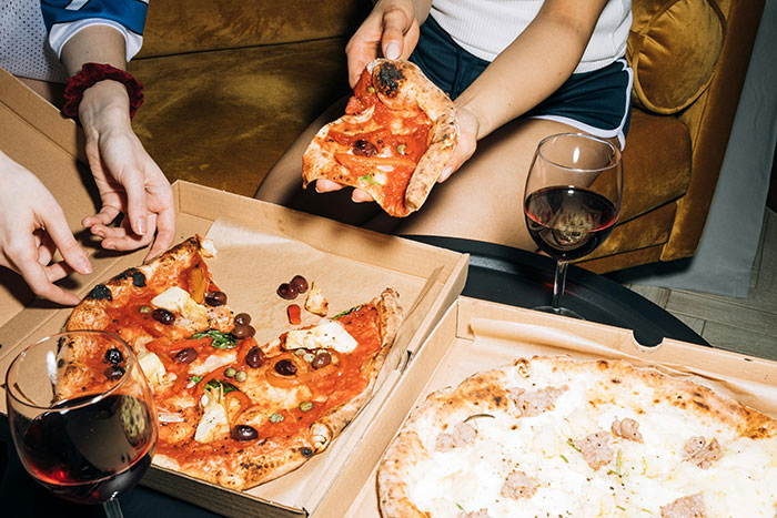 Woman enjoying pizza dinner with friends, featuring slices and wine on a cozy table setting. Woman enjoying pizza dinner with friends, featuring slices and wine on a cozy table setting.