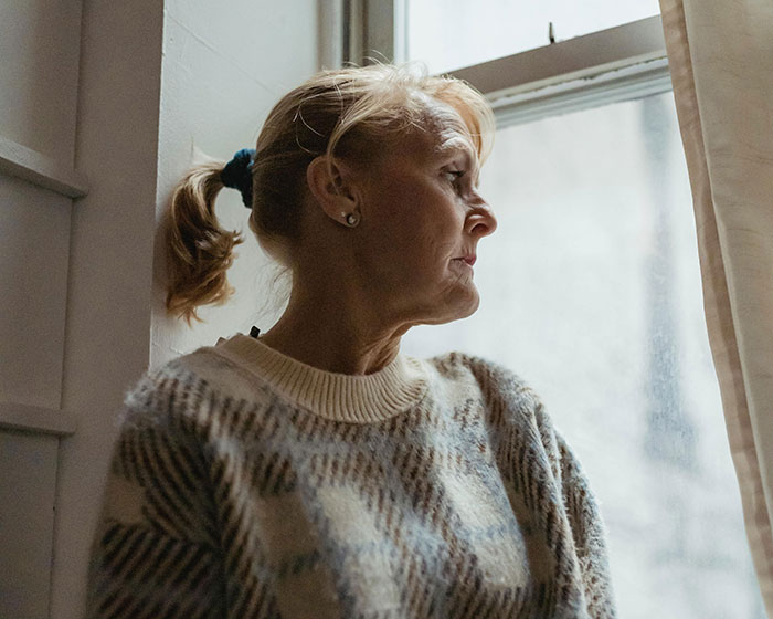 Woman planning dinner alone, looking out a window pensively. Woman planning dinner alone, looking out a window pensively.
