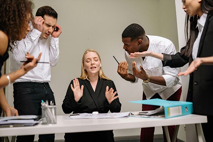 Group in heated discussion around a table, a woman appears troubled as others debate her "tragic story of shattered dreams.