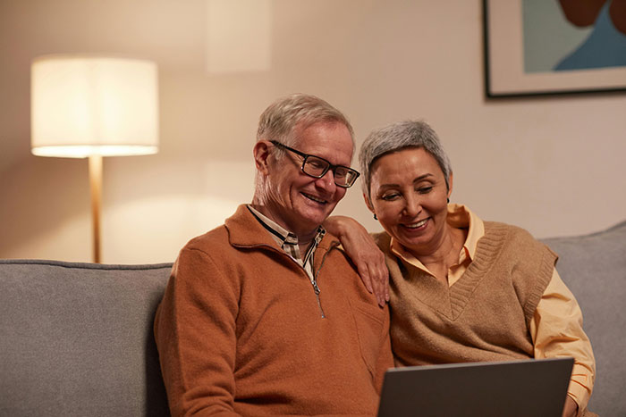 Elderly couple on a couch, smiling and looking at a laptop, discussing a daughter's story.