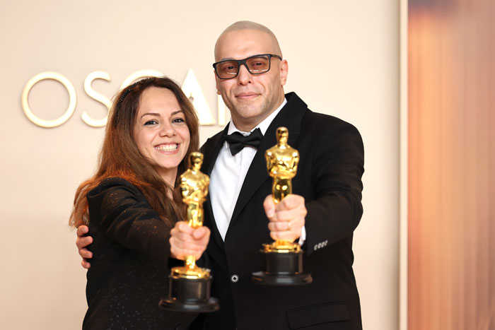 Two Oscar winners holding their trophies, smiling and wearing formal attire at the Oscars 2025.