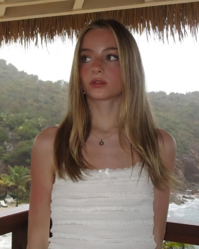 Teen daughter of Naomi Watts by a scenic view, wearing a white top.