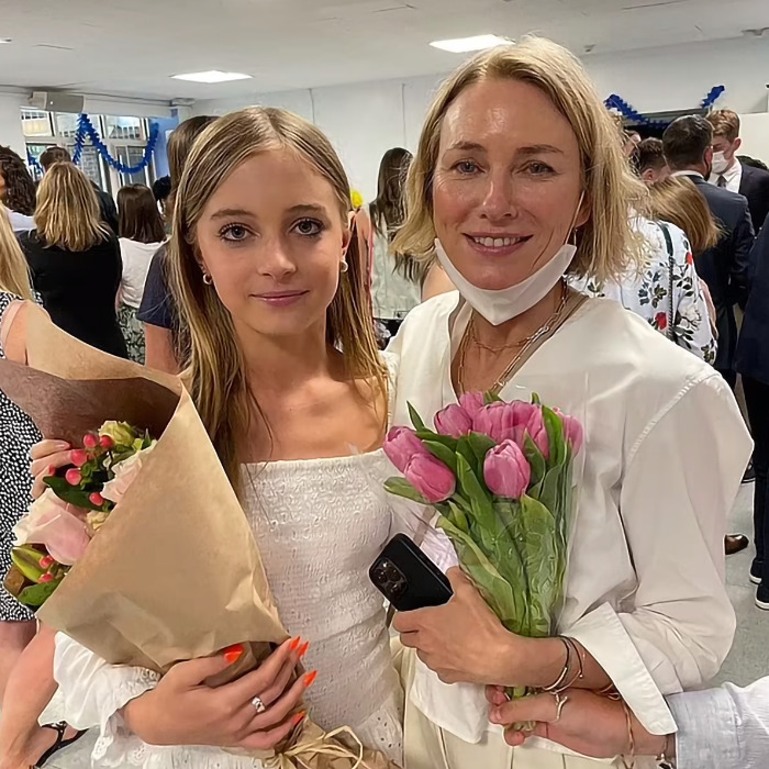 Mother and daughter holding flowers, posing together at an indoor event.