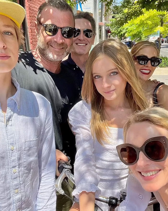 Group selfie outdoors, including Naomi Watts and others, with her teen daughter in the center wearing a white blouse.