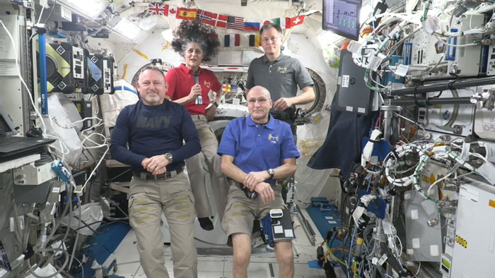 SpaceX crew arrives at ISS to assist stranded NASA astronauts, seated in the space station interior with equipment in view.