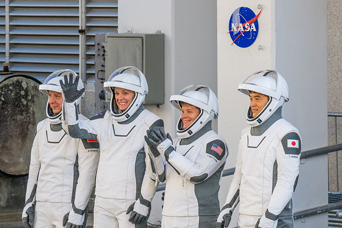 Astronauts in SpaceX suits smiling and waving near NASA emblem, involved in delayed rescue mission. Astronauts in SpaceX suits smiling and waving near NASA emblem, involved in delayed rescue mission.