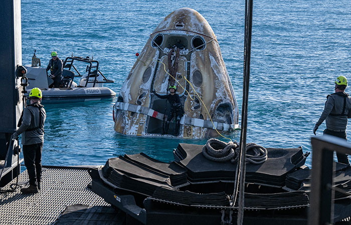 Doctors aiding stranded astronauts during a capsule recovery operation at sea, surrounded by rescue crew and boats.
