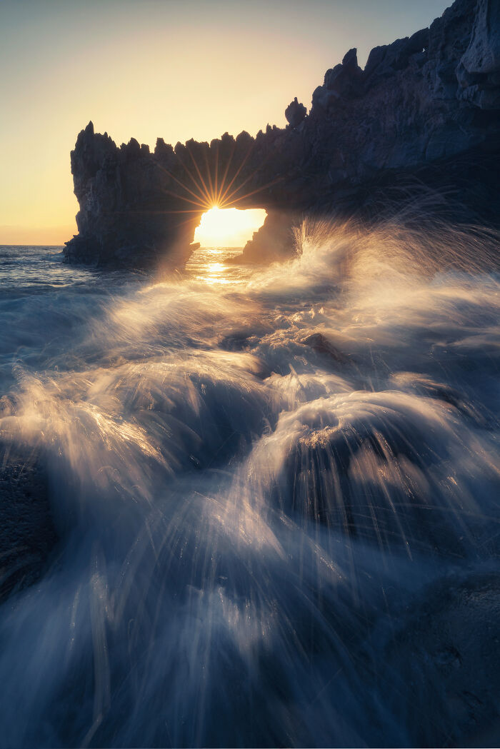 Stunning landscape photo of ocean waves crashing against a rocky arch at sunset.