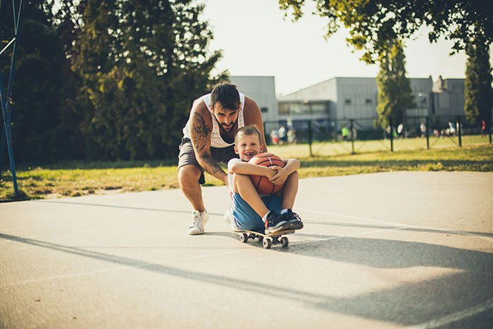Adult guiding a child on a skateboard, demonstrating negative reinforcement to help kids overcome fears in a park setting.