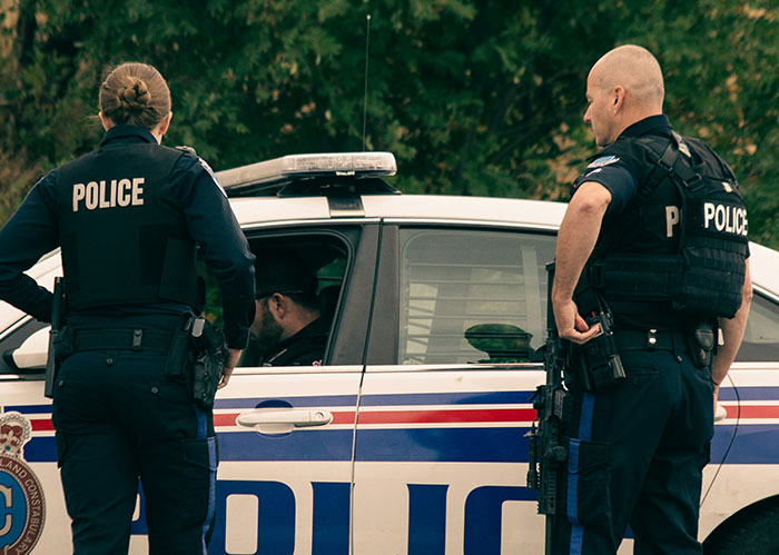 Police officers standing by a patrol car, discussing a situation related to an unhinged neighbor story. Police officers standing by a patrol car, discussing a situation related to an unhinged neighbor story.