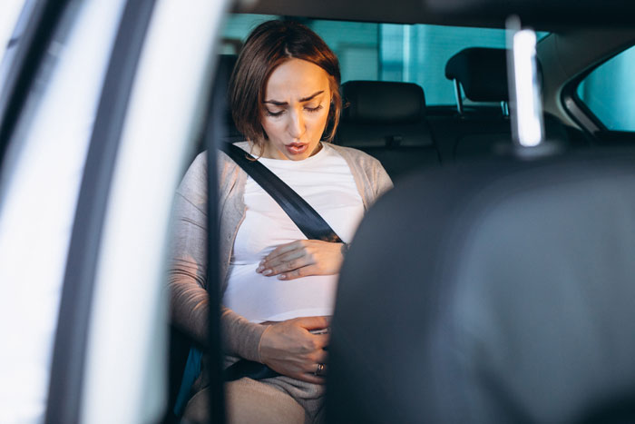Pregnant neighbor in car, clutching belly, prepared for ride with waterproofed seats for protection. Pregnant neighbor in car, clutching belly, prepared for ride with waterproofed seats for protection.