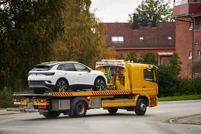 Yellow tow truck carrying a car parked in a disabled spot on a residential street.