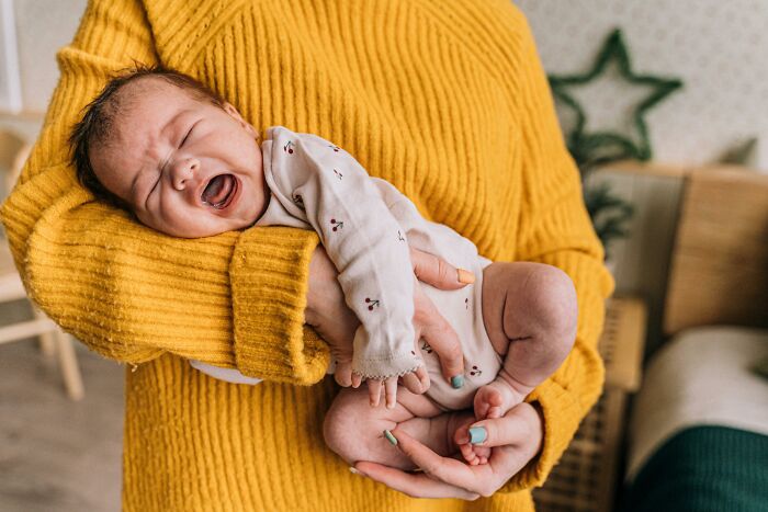 A woman in a yellow sweater holds a crying baby, prioritizing baby's health over other commitments.