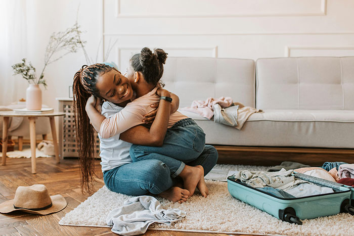 Mother and child hugging in living room with open suitcase, child's unwanted feelings theme. Mother and child hugging in living room with open suitcase, child's unwanted feelings theme.