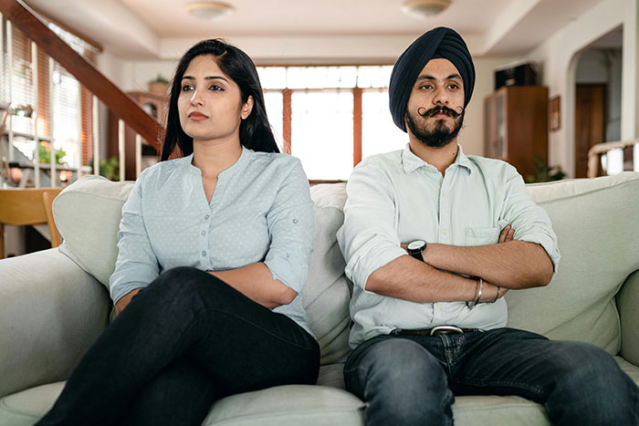 Couple sitting on a couch with serious expressions, conveying tension related to family dynamics and feeling unwanted. Couple sitting on a couch with serious expressions, conveying tension related to family dynamics and feeling unwanted.