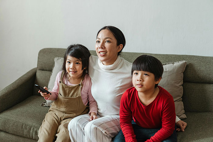 Mom with two kids on a couch, watching TV together, capturing a family moment. Mom with two kids on a couch, watching TV together, capturing a family moment.