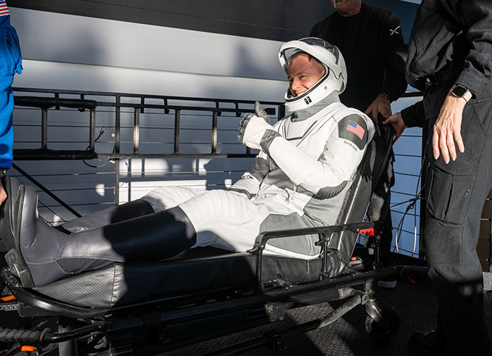 Astronaut in a spacesuit on a stretcher, assisted by doctors, raising concern over stranded astronauts.