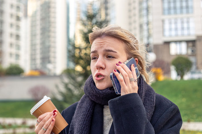 Woman talking on phone outdoors, holding a coffee cup, depicting aunt flipping the script on sticky-fingers niece scenario.