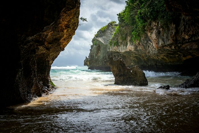 Rocky coastline with waves crashing against stunning beach cliffs under a cloudy sky.