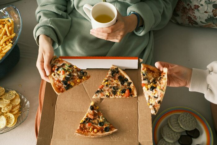 Person enjoying pizza slices at home, possibly winners of a lifetime supply, with snacks and tea nearby.