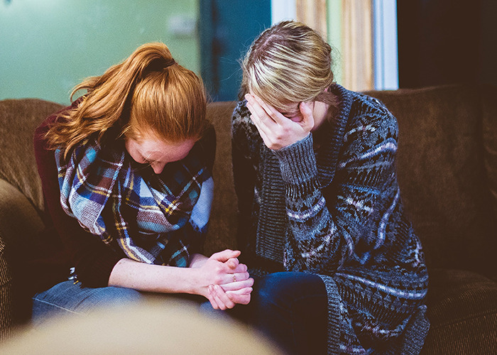 Two women sitting on a couch, showing emotional distress, highlighting childhood trauma experiences.