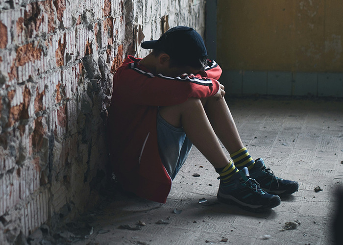Child sitting alone in a dim room, head down, illustrating childhood traumatic experience.
