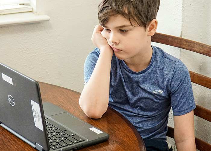 Child looking at a laptop, appearing thoughtful and slightly bored, evoking memories of past childhood experiences.
