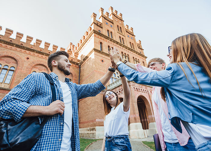 Group of friends high-fiving in front of a historic building, reminiscent of mom groups' tight-knit bonds.