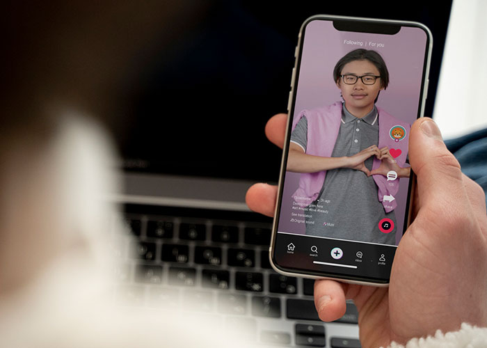 Person using phone to watch a video, wearing glasses and making a heart sign, as part of mom groups content.