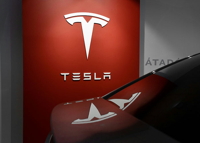 Tesla logo on a red wall with a car hood, similar to modern community group branding.