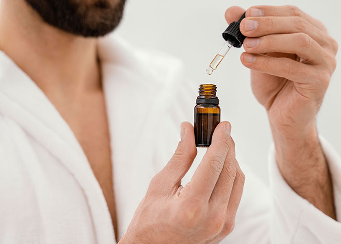 Man in a robe using a dropper with an oil bottle, highlighting a comforting home ritual moment.