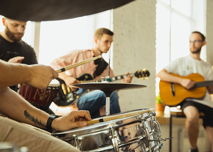 Musicians jamming in a bright room, playing drums and guitars, creating a lively atmosphere similar to mom groups.