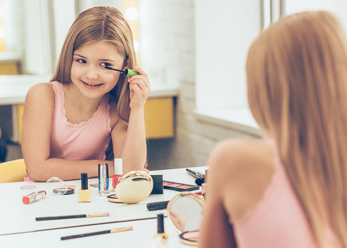 A young girl applying makeup at a vanity, mimicking adult routines in a playful setting.