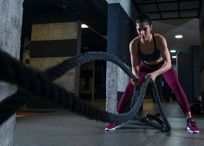 Woman in a gym using battle ropes for an intense workout session.