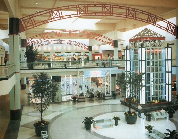 Vintage mall interior with colorful arches, plants, and seating, evoking nostalgic food court memories.