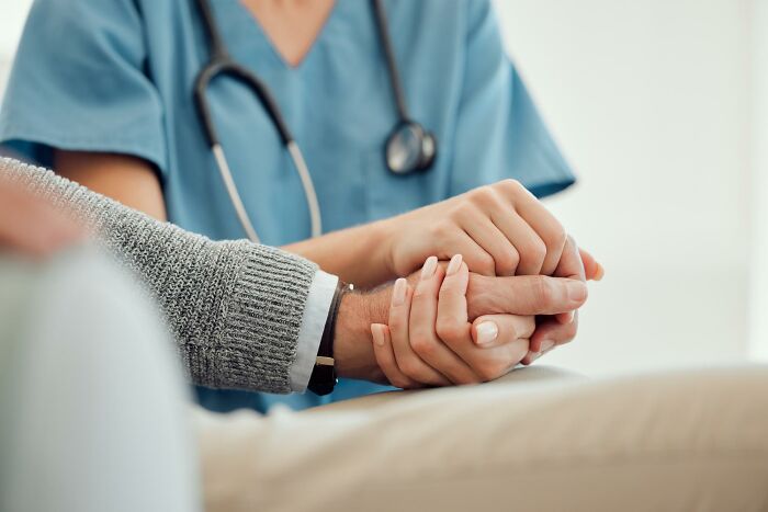 A healthcare professional holds a patient's hand, illustrating normal supportive care in society.