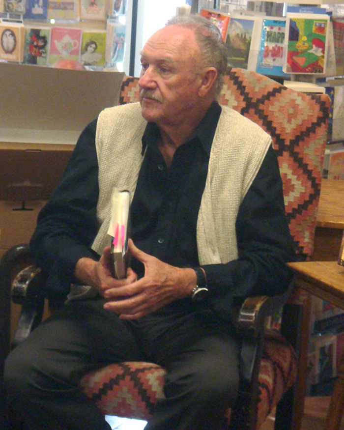 Man seated with a book, wearing a vest and dark shirt, in a room with colorful wall art. Man seated with a book, wearing a vest and dark shirt, in a room with colorful wall art.