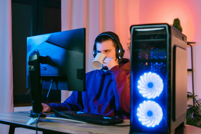 Person in hoodie with headphones, sipping coffee, working at a computer; challenging job misconceptions.