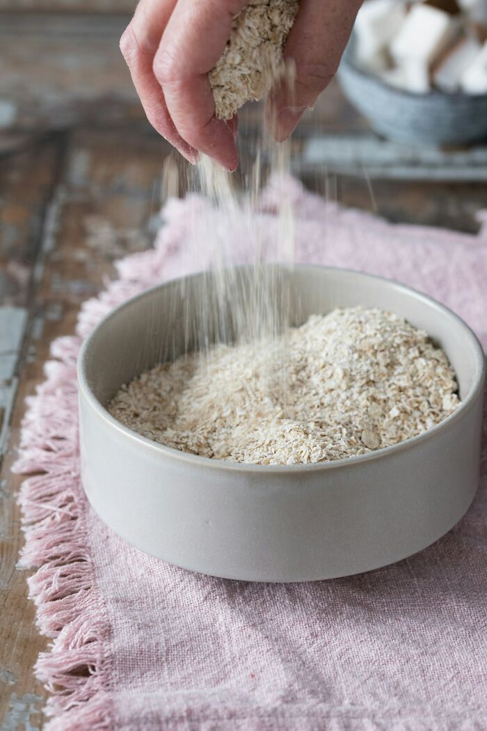 Hand sprinkling oats into a bowl on a pink cloth, symbolizing a disappointing job bonus.