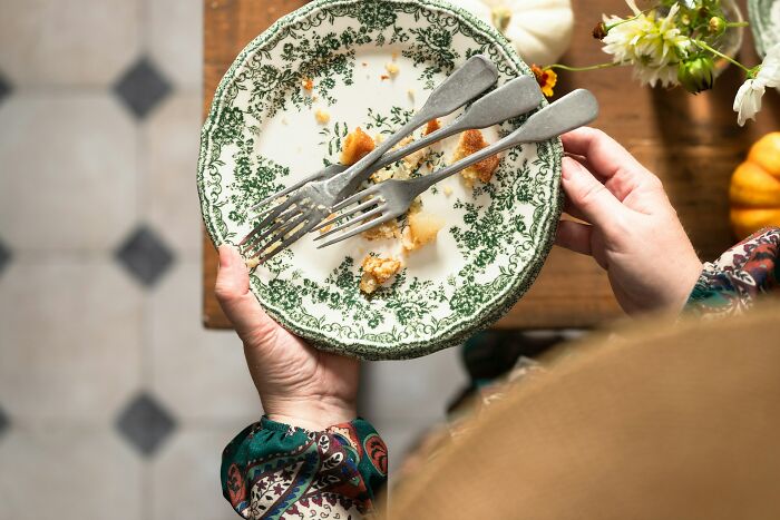 A person holding a vintage plate with crumbs and forks, highlighting historical dining remnants.