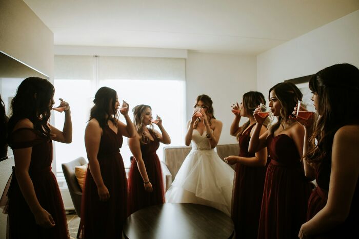 Bridesmaids and bride sipping drinks in a room, dressed for a wedding.