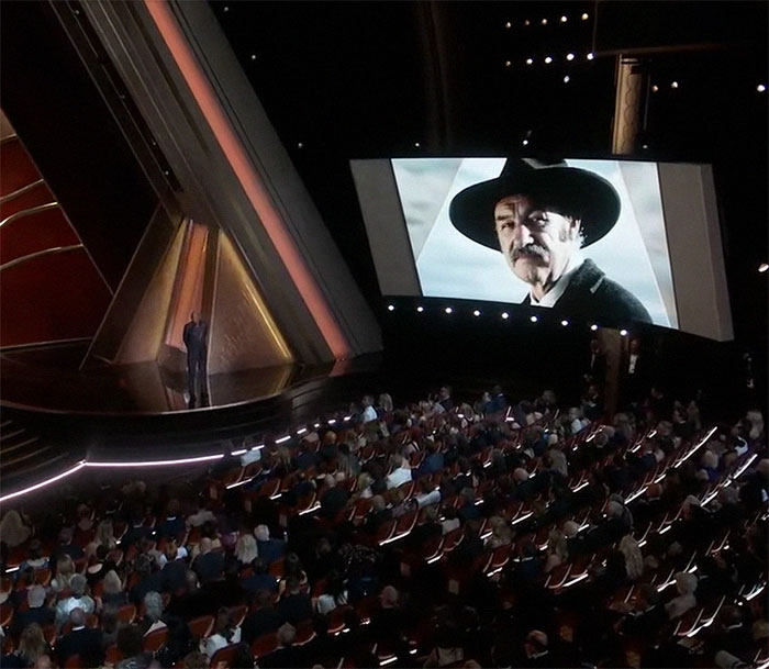 Oscars ceremony audience watching In Memoriam tribute on a large screen, highlighting event significance.