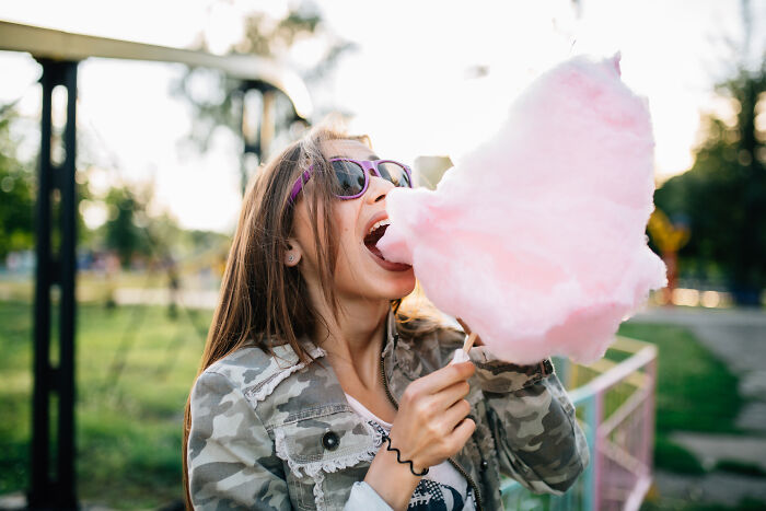 Woman in sunglasses enjoying pink cotton candy outdoors, highlighting diverse food preferences.