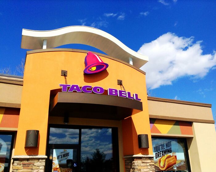 Taco Bell storefront with iconic bell logo under a clear blue sky, related to hyped fast foods.
